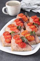 Homemade sandwiches with turkey pate and cherry tomatoes, also a cup of coffee on gray background