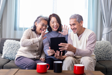 Asian family reunion of senior father mother and daughter sitting on couch with happy smile in retirement home while having video call to others relation and cousin member - obrazy, fototapety, plakaty