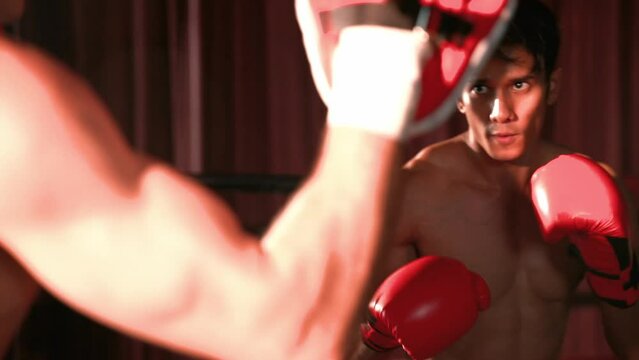 Asian and Caucasian Muay Thai boxer unleash punch in fierce boxing training session, delivering punching strike to sparring trainer, showcasing Muay Thai boxing technique and skill. Impetus