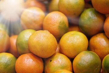 Ripe oranges or tangerines with a flare from the sun's rays. Sun flare blur against pile of fresh tangerines, juicy citrus, texture blurred background. Christmas, New Year mood, symbol of good luck