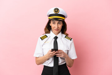 Airplane middle aged pilot woman isolated on pink background surprised and sending a message