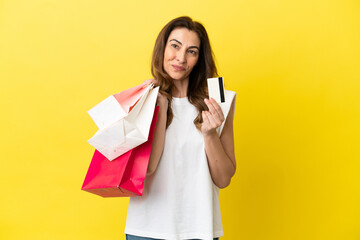 Middle aged caucasian woman isolated on yellow background holding shopping bags and a credit card