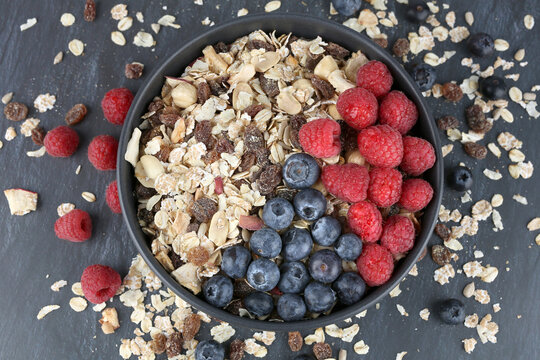 Muesly with raspberries and blueberries in black bowl on dark background.
