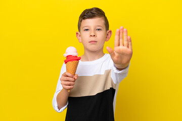 Little caucasian boy with a cornet ice cream isolated on yellow background making stop gesture