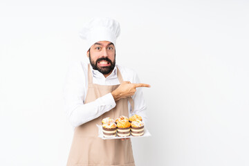 Young man holding muffin cake over isolated white background frightened and pointing to the side