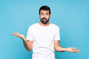 Young man with beard  over isolated blue background unhappy for not understand something