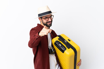 Traveler man man with beard holding a suitcase over isolated white background points finger at you with a confident expression