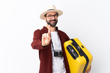 Traveler man man with beard holding a suitcase over isolated white background showing and lifting a finger