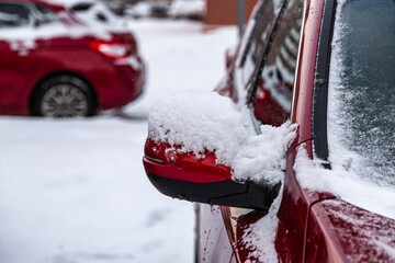 Snow covered red car mirror in winter