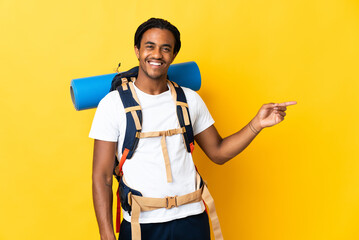 Young mountaineer man with braids with a big backpack isolated on yellow background pointing finger to the side and presenting a product