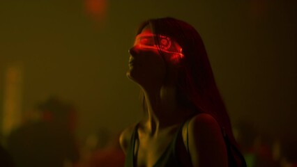 Young woman in futuristic neon glasses at cyberpunk style party in techno club. Sensually dancing girl in glowing goggles moves to music beat in crowd of people. Cyber city nightclub, concept - Powered by Adobe