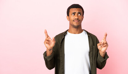 African American man on copyspace pink background with fingers crossing and wishing the best