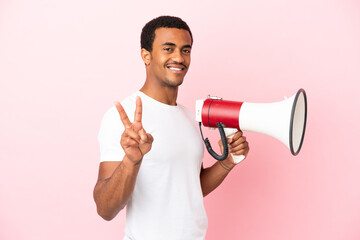 African American handsome man on isolated pink background holding a megaphone and smiling and...
