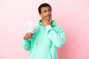 Young man taking a lot of money over isolated pink background having doubts