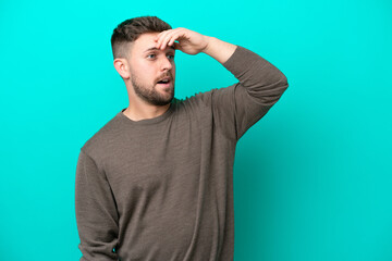 Young caucasian man isolated on blue background doing surprise gesture while looking to the side