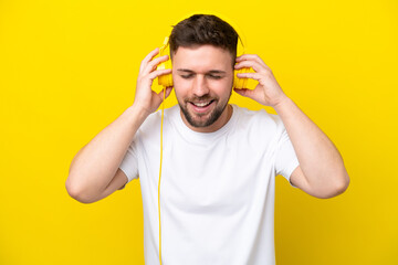 Young caucasian man isolated on yellow background listening music