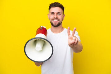 Young caucasian man isolated on yellow background holding a megaphone and smiling and showing...