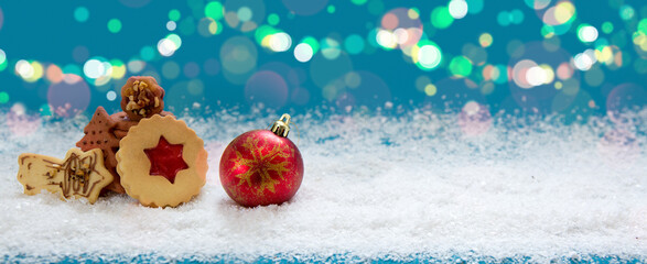 Christmas cookies and red ball on white snow isolated on blue background.