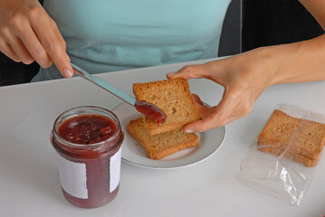Female hand spreading jam on toasted bread slice.