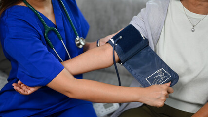 Healthcare worker measuring blood pressure middle age woman during home visit. Home health care...