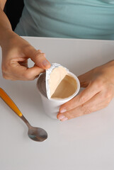 Woman hand opening yogurt container on kitchen table.