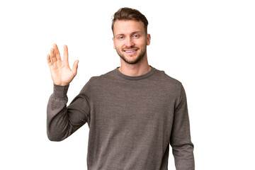 Young handsome caucasian man over isolated chroma key background saluting with hand with happy...