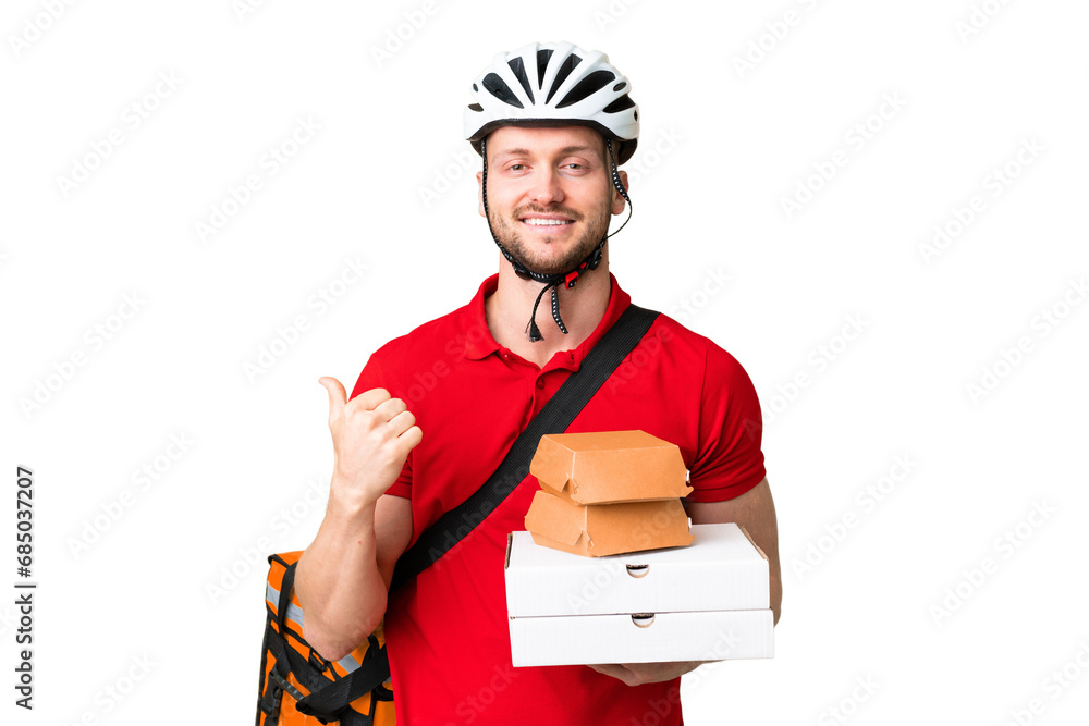 Wall mural Young delivery man taking a takeaway food over isolated chroma key background pointing to the side to present a product