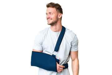 Young caucasian man with broken arm and wearing a sling over isolated chroma key background looking...