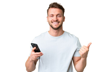 Young handsome caucasian man over isolated chroma key background using mobile phone while doing thumbs up