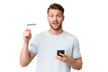 Young handsome caucasian man over isolated chroma key background buying with the mobile and holding a credit card with surprised expression
