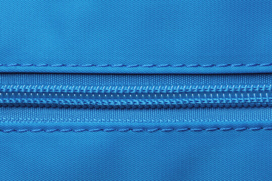 Zip fastener background texture. A high-resolution close-up of a detail from a closed plastic zip fastening on a backpack made of an elastic blue nylon fabric. Macro photo.