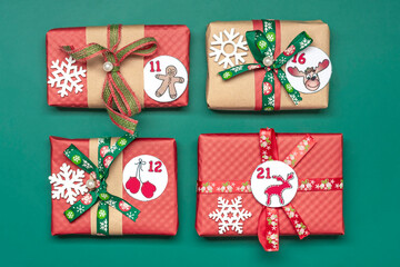 Handmade wrapped red, green gift boxes decorated with ribbons, snowflakes and numbers, Christmas decorations and decor on green table Xmas advent calendar concept Top view Flat lay Holiday card