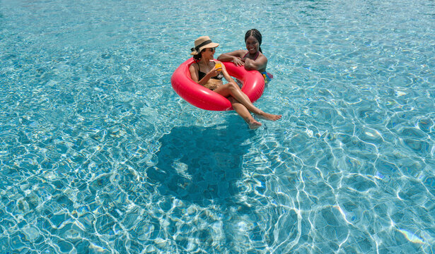Two ladies in bikini are joyfully floating together on a big inflatable ring in blue water.