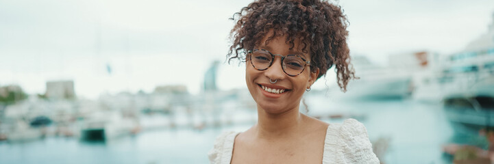 Closeup portrait of a young woman in glasses stands in the seaport and poses for the camera