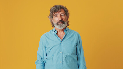 Elderly gray-haired bearded man wears a blue shirt, looks at the camera, isolated on an orange...
