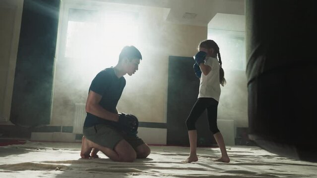 Child kicks pad under trainer control in gym. Combat trainer works with little girl upon leg attack in sports club slow motion. Martial arts school