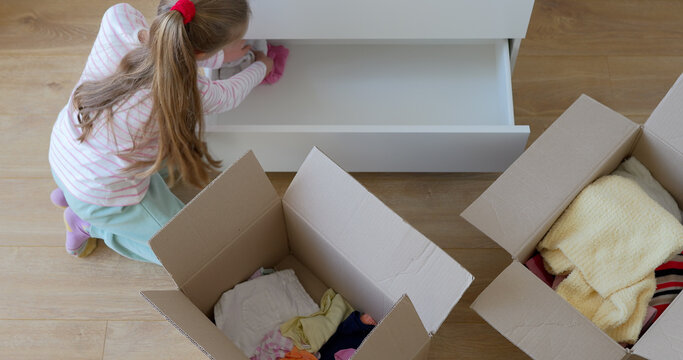 Little girl putting clothes to drawer in bedroom after moving