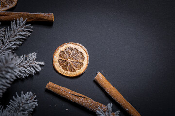 A piece of dried orange on a dark background among cinnamon and snow-covered Christmas tree branches
