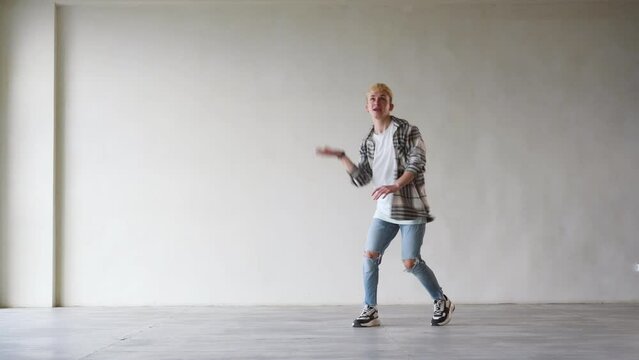 Laughing young man dancer in casual dancing in front of wall. People emotions lifestyle concept. Mock up copy space.