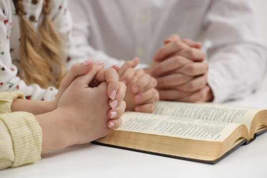 Girl and her godparent praying over Bible together at table indoors, closeup