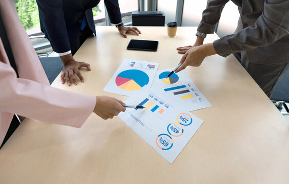A group of business professional are huddled together around a table, concentrating on various graph and data visualization.