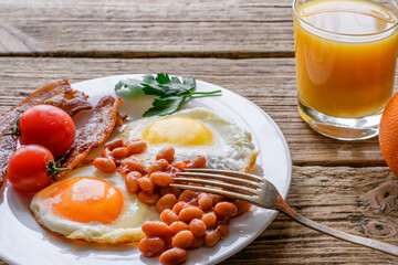 Full english breakfast with eggs, bacon, beans, tomatoes and orange juice in a plate with fork on...
