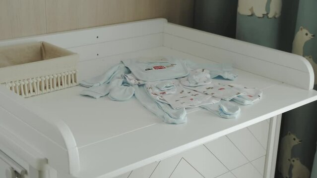 Close-up view of white wooden changing table. Changing table with newborn blue colored clothes for baby boy, slow motion.
