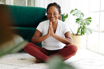 Mental wellbeing with yoga: Senior woman meditating at home