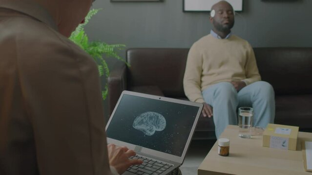 Female doctor typing on laptop and examining activity of patient brain displayed on screen during sleep test in clinic