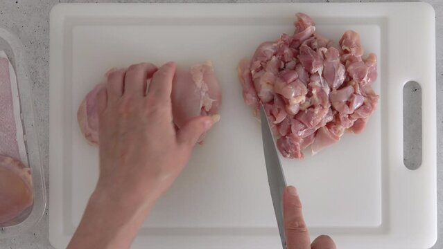 The woman cuts raw boneless skinless chicken thighs into cubes. Marinated chicken fillet recipe