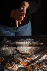 Top view of woman's hands with flour on dark table with gingerbread cookie dough with rolling pin,...