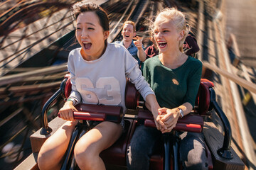Happy young people riding a roller coaster - obrazy, fototapety, plakaty