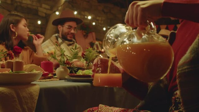 Unrecognizable woman pouring orange juice from glass jug at festively set dining table in backyard during Day of the Dead celebration