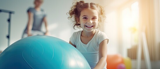 Girl receiving physiotherapy in a children s therapy center doing exercises on a gymnastic ball with physiotherapists for scoliosis prevention and treatment copy space image - obrazy, fototapety, plakaty